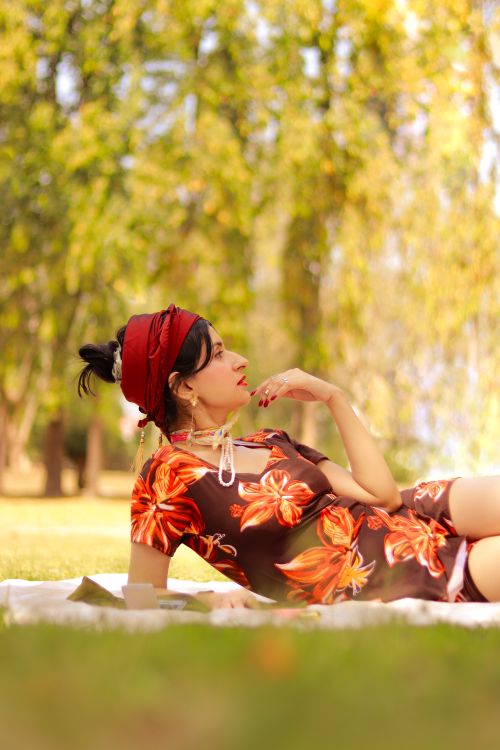 Free Woman in vibrant floral attire relaxing in a sunlit park. Perfect for lifestyle and fashion themes. Stock Photo