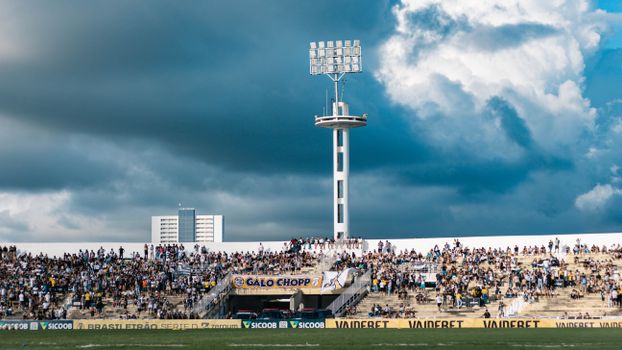 Lively football match crowd in stadium with dramatic clouds overhead.