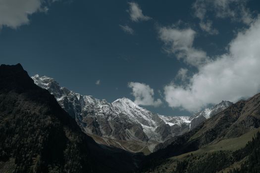 Stunning view of snow-capped mountains under a clear blue sky with scattered clouds.