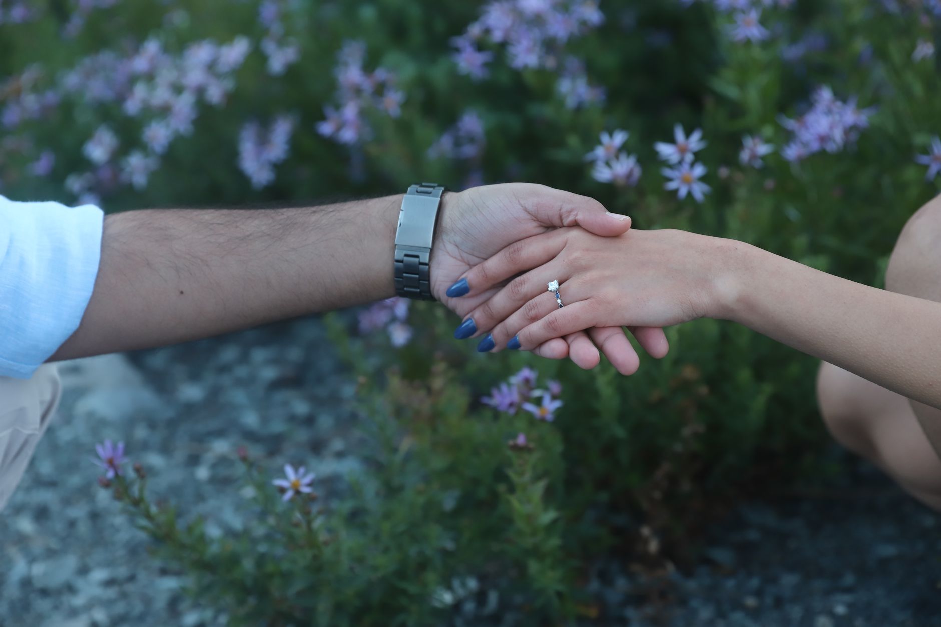 Komitmen Standar Pelayanan dan Dokumentasi Kualitas di Setiap Acara wedding Anda 4 Close-up of engaged couple holding hands in a garden setting with purple flowers.