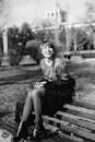 Grayscale Photography of Woman Sitting on Slatted Bench