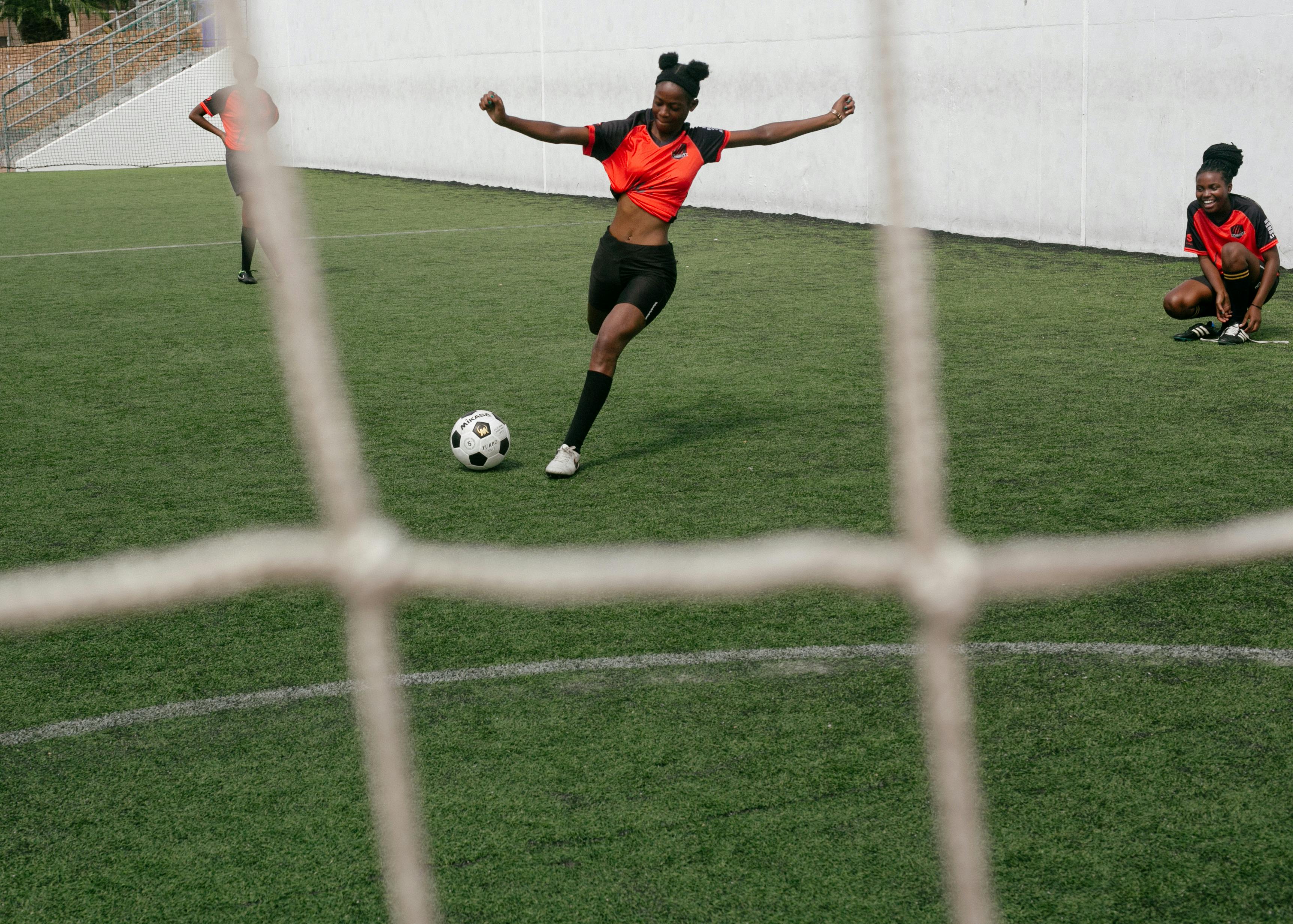 girl in red shirt and black shorts kicking a soccer ball