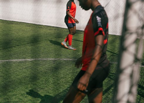 Crop young African American female football player practicing with ball in training in sunny day