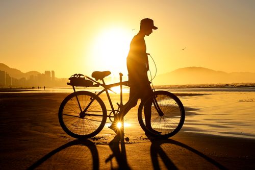 Free Silhouette of a man walking with a bicycle along the beach during a stunning sunset. Stock Photo