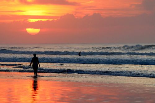 Free Silhouettes of people enjoying a vibrant sunset on a beach with serene waves. Stock Photo