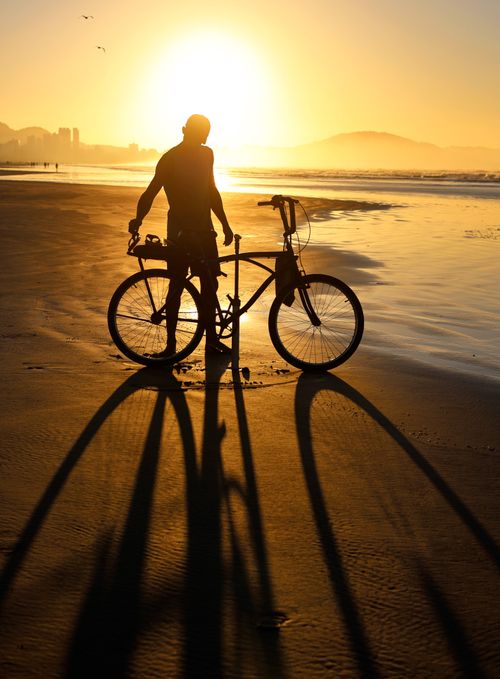 Free Cyclist silhouette on beach with long shadows during golden sunset. Stock Photo