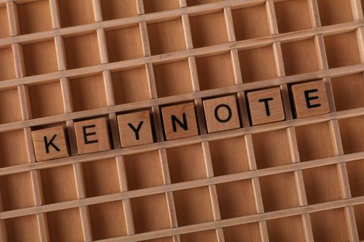 Wooden Scrabble tiles arranged to spell 'KEYNOTE' on a wooden grid background.