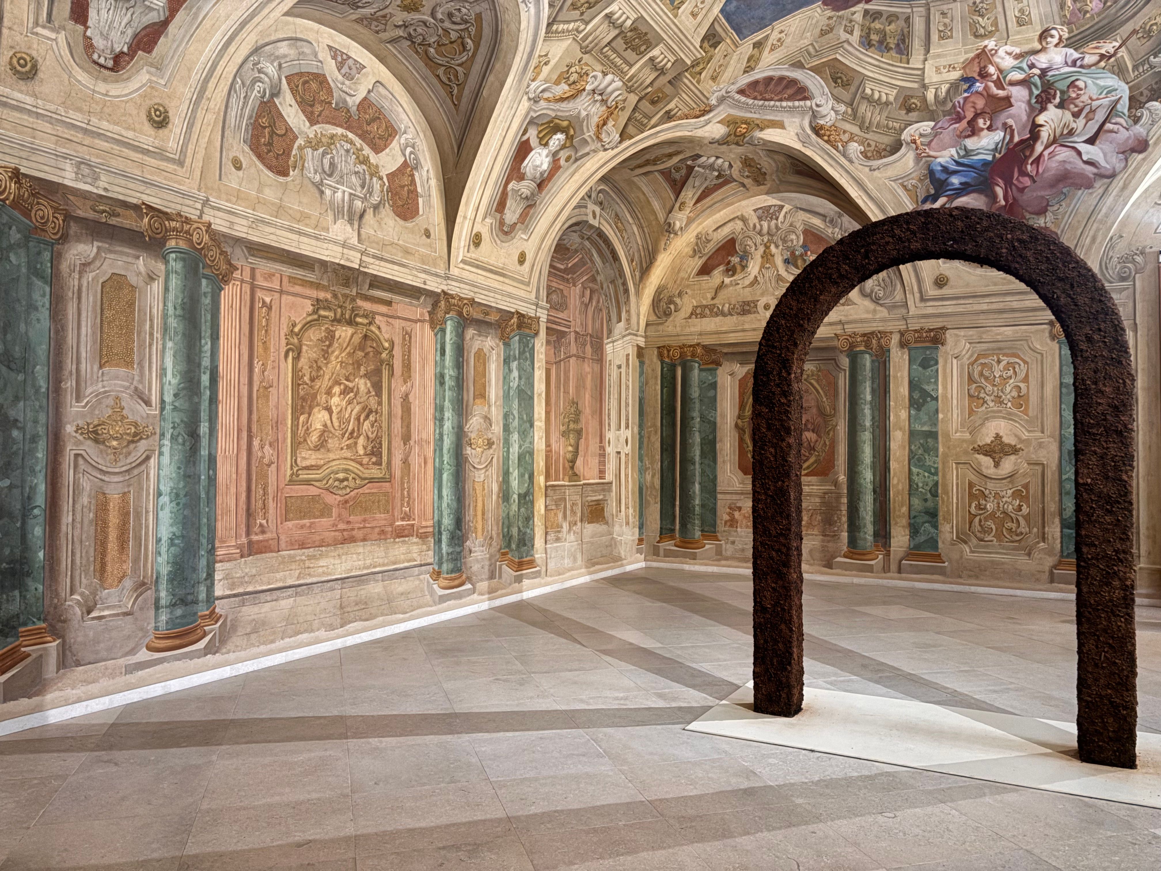 Elegant Baroque room featuring detailed frescoes and a modern arched sculpture.