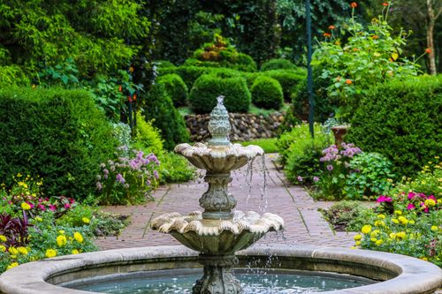 Free A tranquil garden scene featuring a classic stone fountain surrounded by lush greenery and colorful flowers. Stock Photo