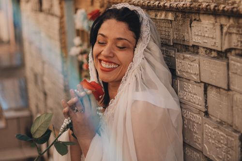 Free Joyful woman with a red rose and lace shawl by a decorated wall. Stock Photo
