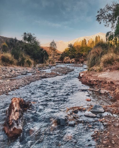 Free Tranquil stream flowing through a mountainous landscape with autumn foliage and snowy peaks. Stock Photo