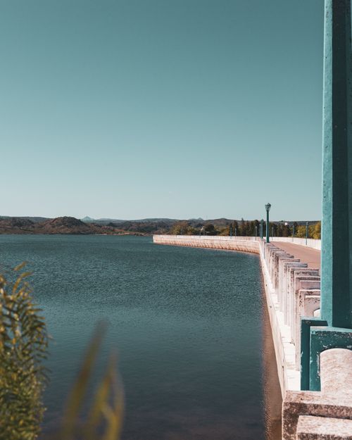 Free A tranquil view of a dam adjacent to a vast lake under a clear blue sky. Stock Photo
