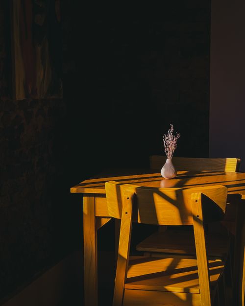 Free Warm sunlight casts shadows on a wooden table with a small vase, creating a cozy indoor atmosphere. Stock Photo