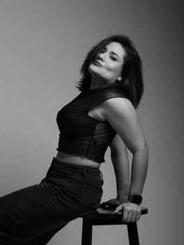 Elegant black and white portrait of a woman seated confidently on a stool.