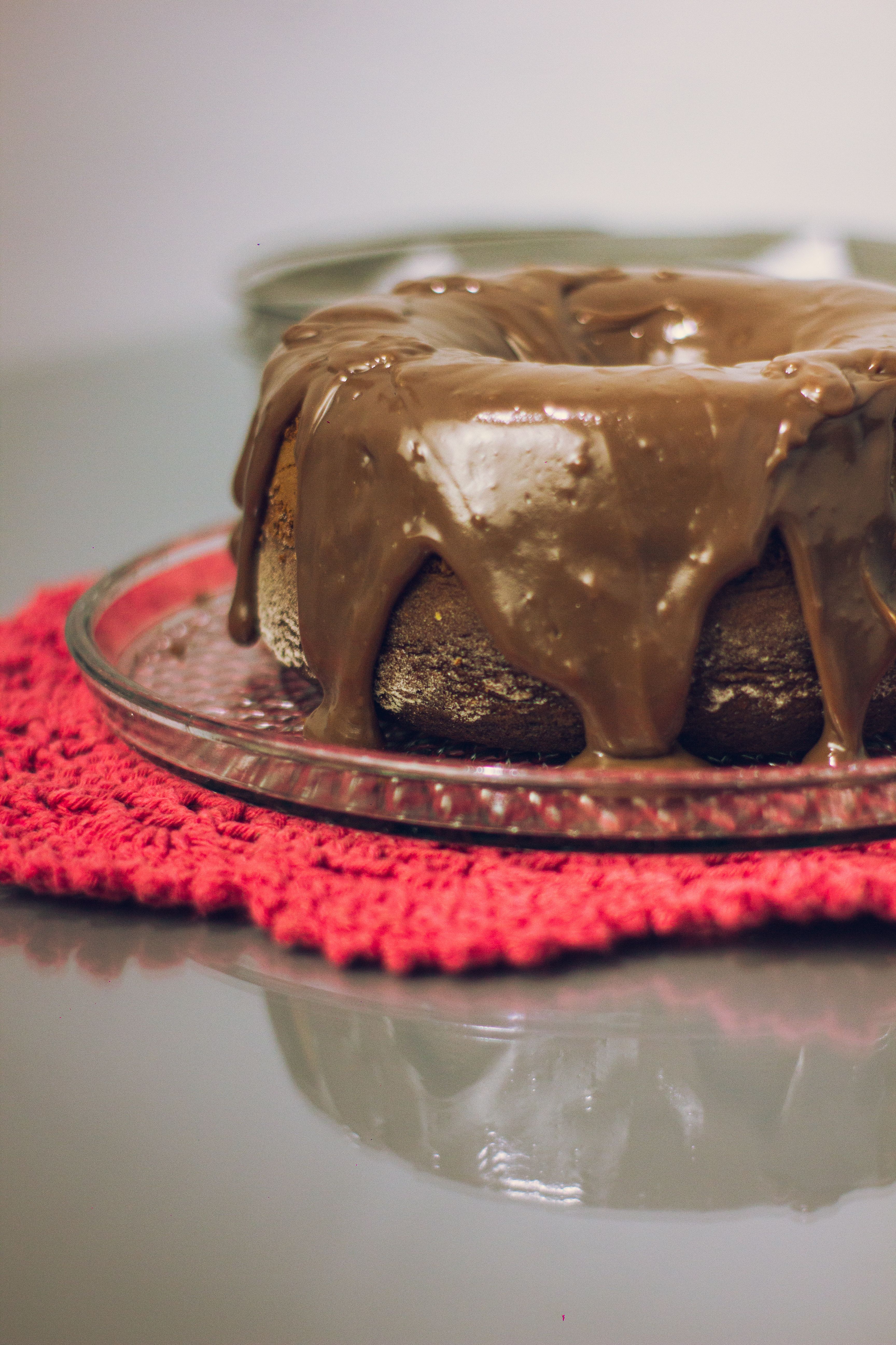 Mouth-watering chocolate bundt cake with rich icing on a glass plate and red crochet mat.