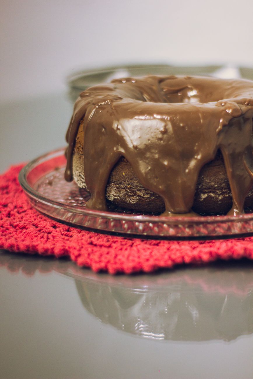 Mouth-watering chocolate bundt cake with rich icing on a glass plate and red crochet mat.