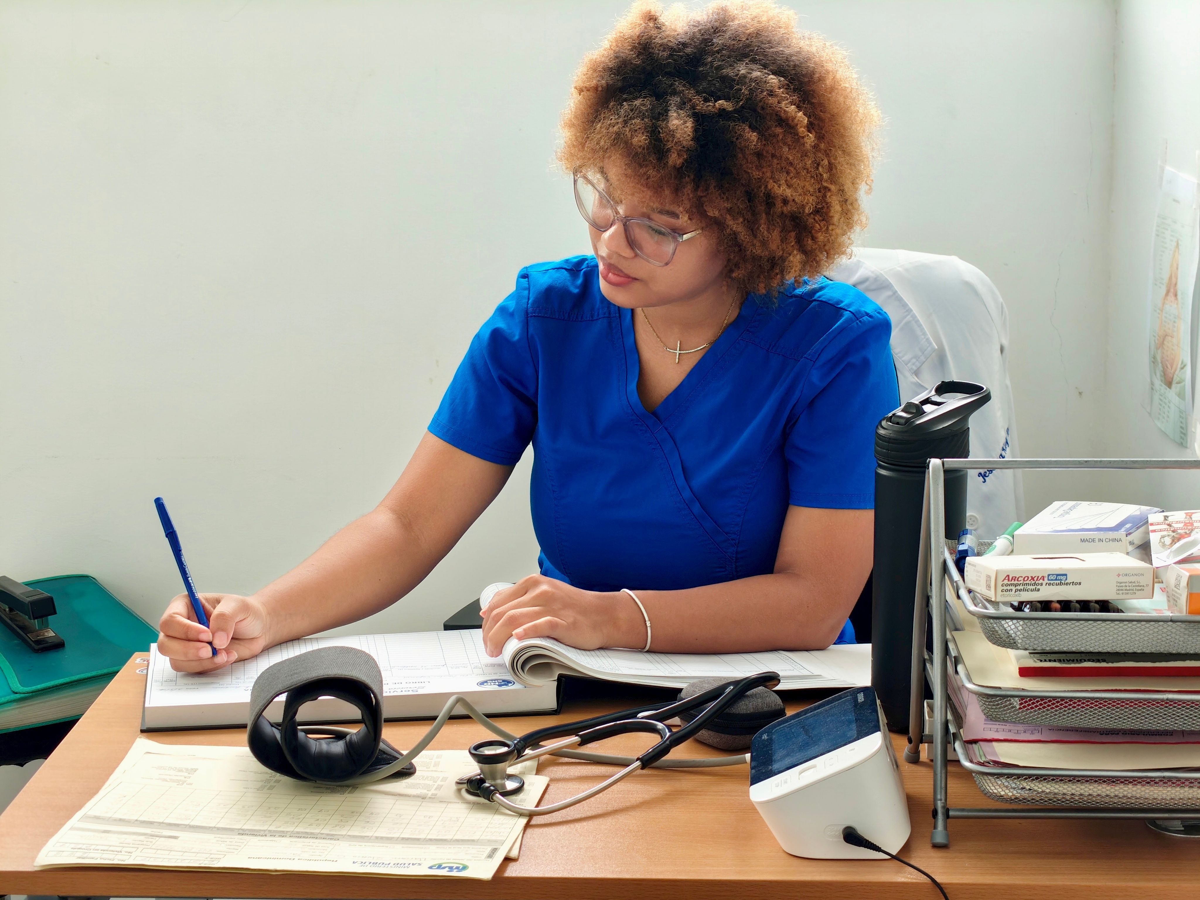 A nurse in blue scrubs writing patient information at a desk with medical equipment. - Evidence evidence guide for berry blood pressure meta-analysis