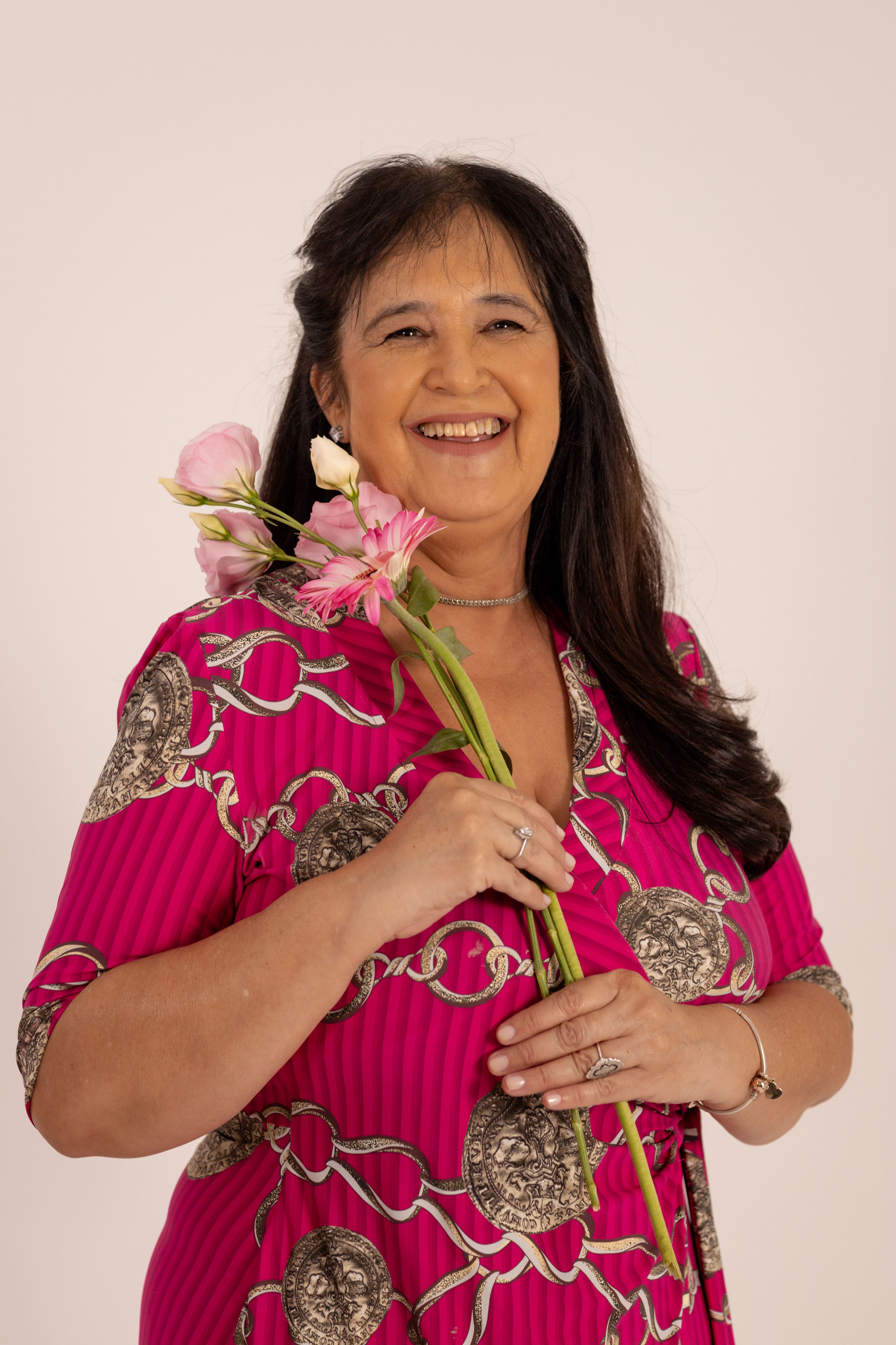 Joyful woman in a pink dress holding pink flowers, smiling in a studio setting.