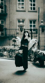 Woman posing in elegant gown with city architecture backdrop, offering a dramatic and stylish urban scene.