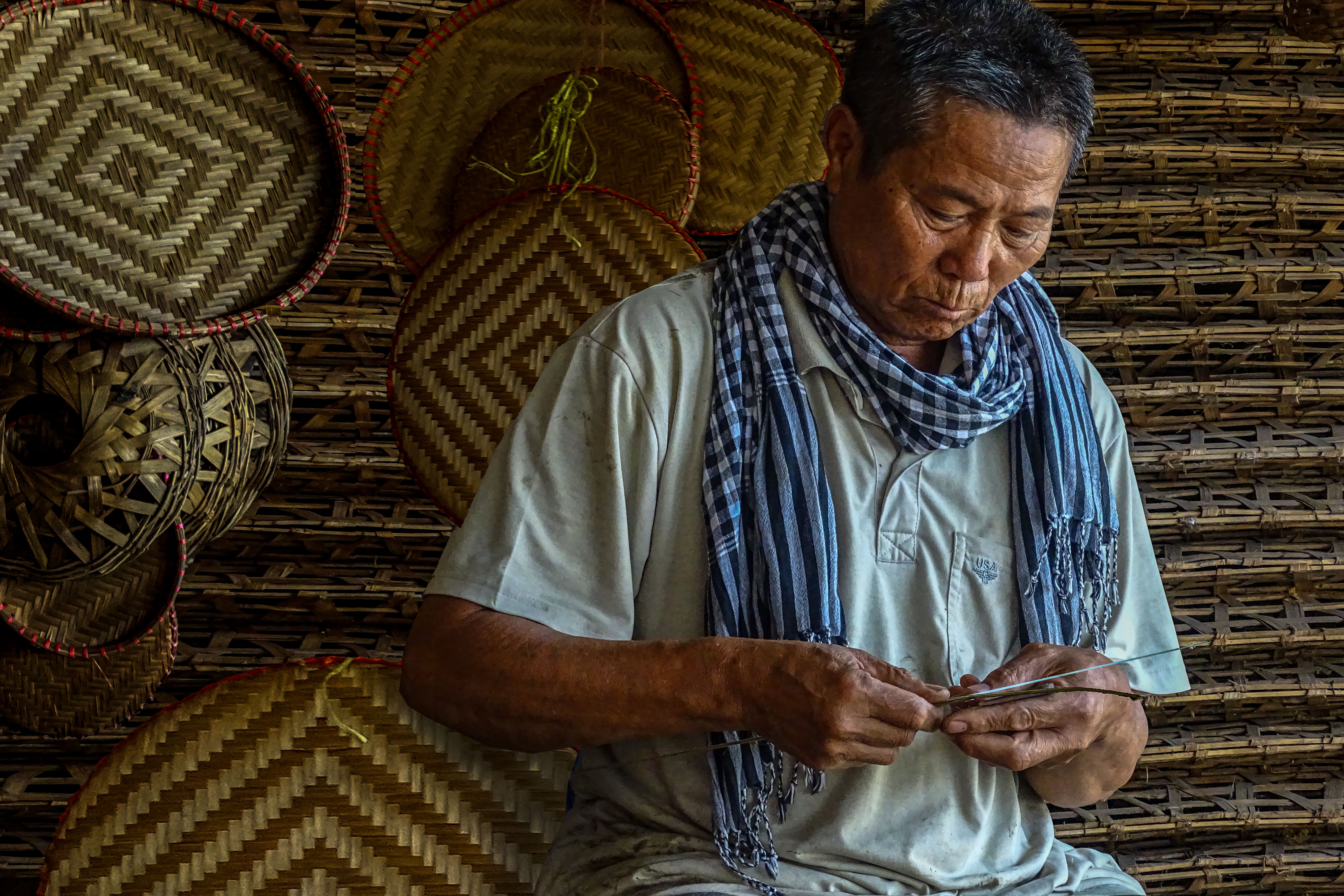 Elderly man skillfully weaving bamboo baskets, showcasing traditional craftsmanship.