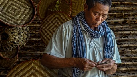 Elderly man skillfully weaving bamboo baskets, showcasing traditional craftsmanship.