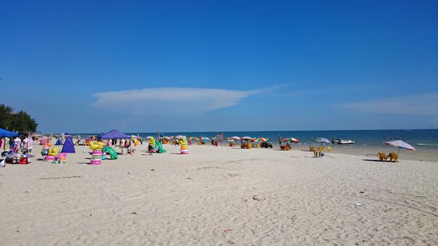 A vibrant beach with colorful umbrellas, people, and calm blue sea.