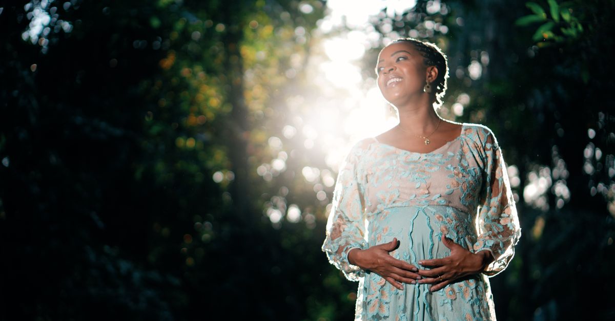 A serene pregnant woman in a sunlit garden wearing a floral dress.