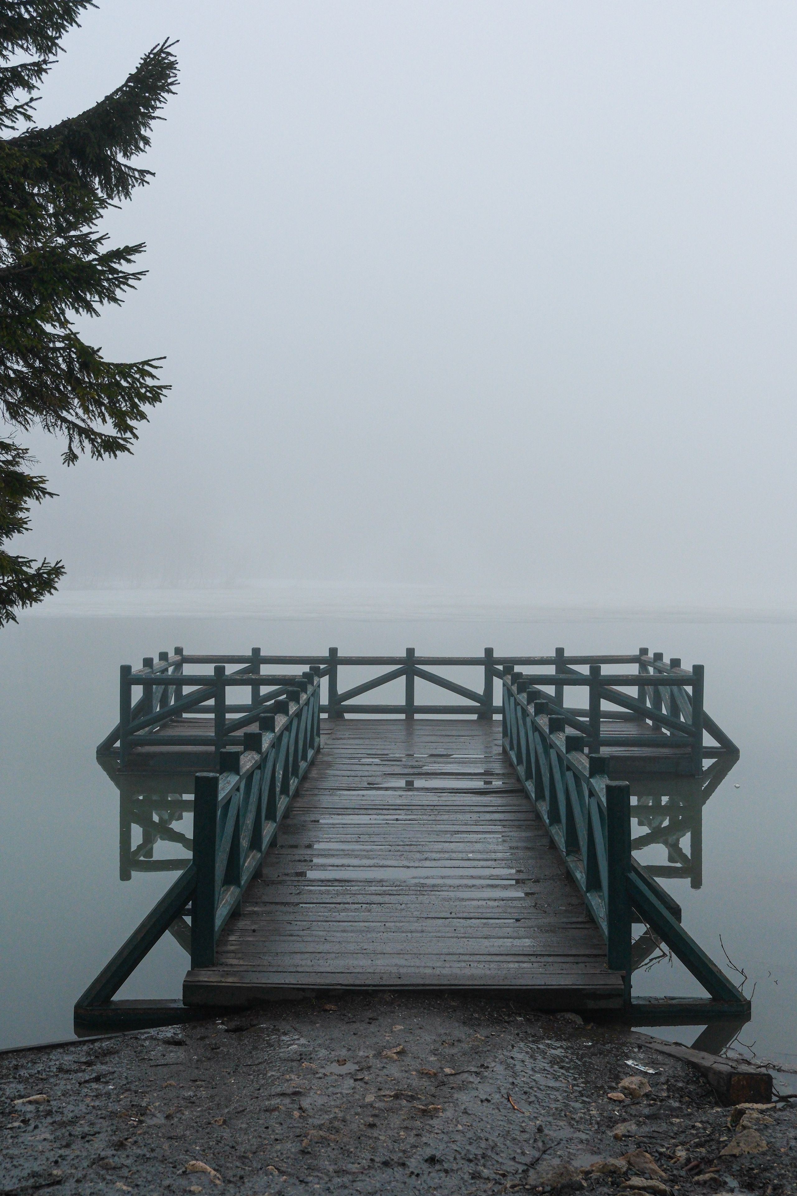 A serene dock extends into a foggy lake surrounded by mist, evoking a calm and peaceful atmosphere.