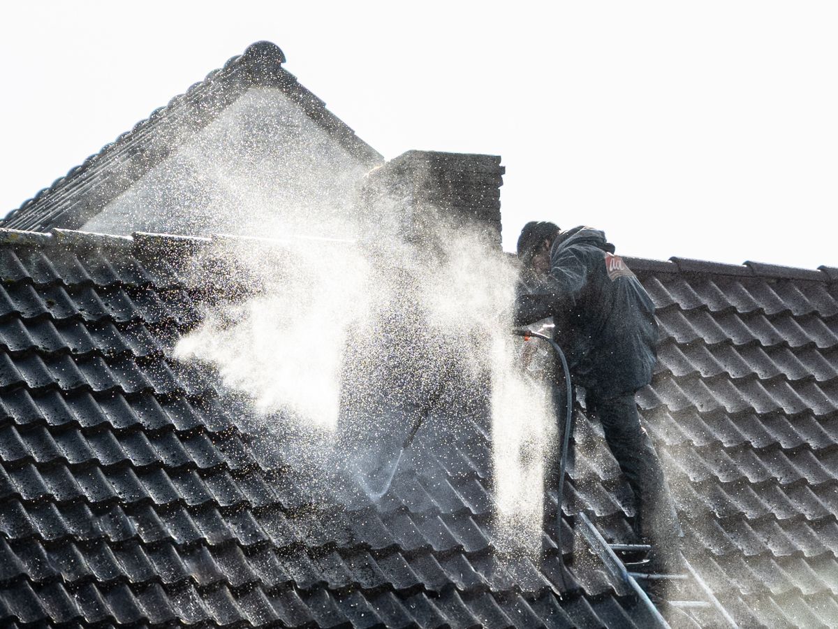 A worker power washing dirty roof tiles with a high pressure water wand.