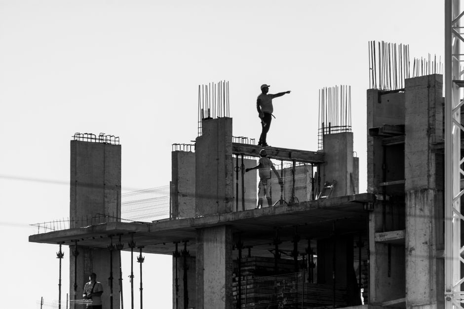 Silhouette of construction workers on a building site with one pointing towards the distance.