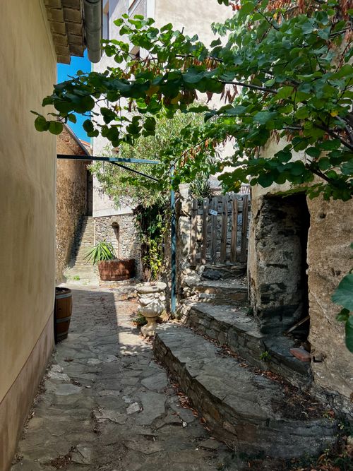 Free A picturesque view of a rustic stone alleyway with lush greenery in a quaint European village. Stock Photo