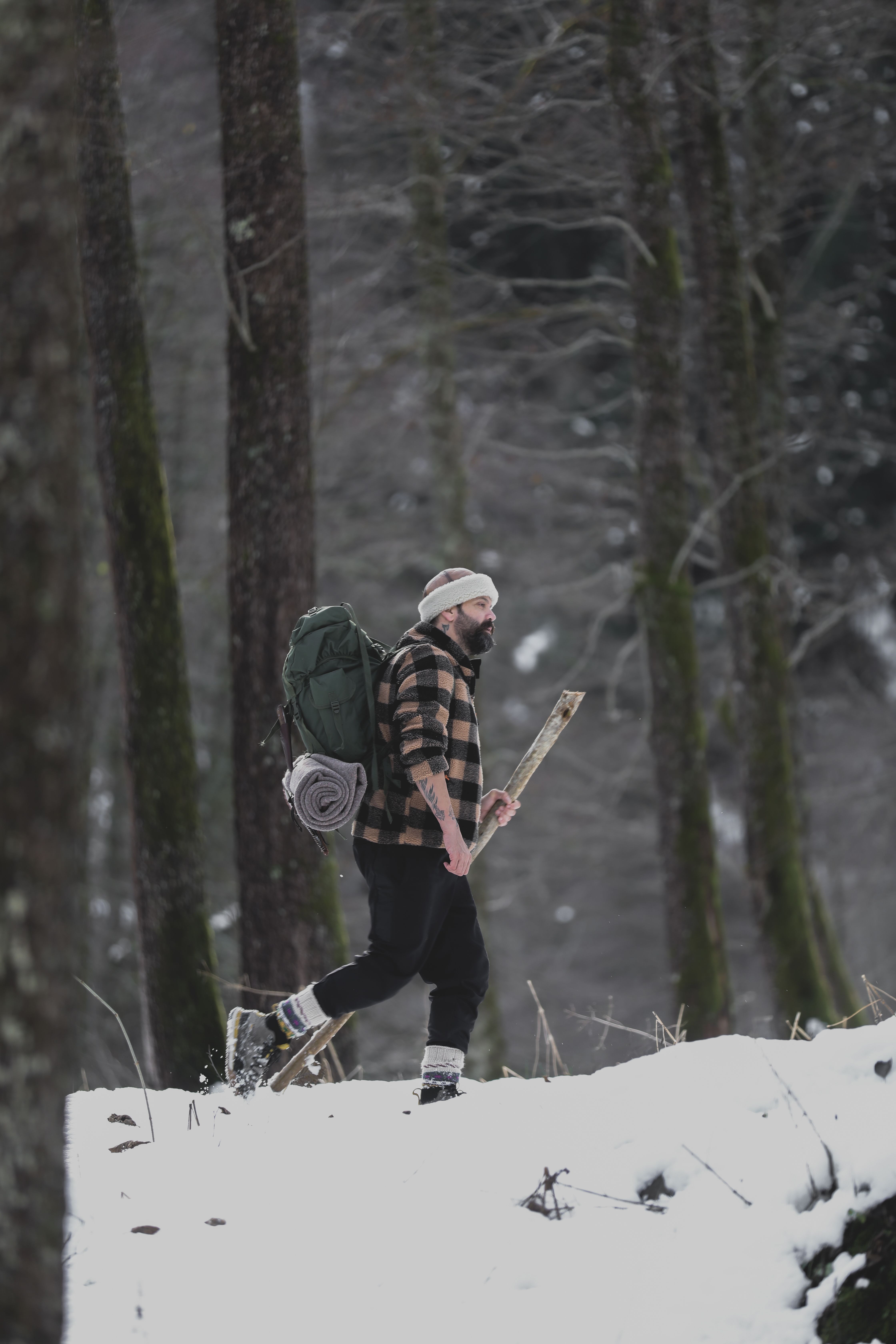 A man hiking through a snowy forest carrying a backpack and stick.