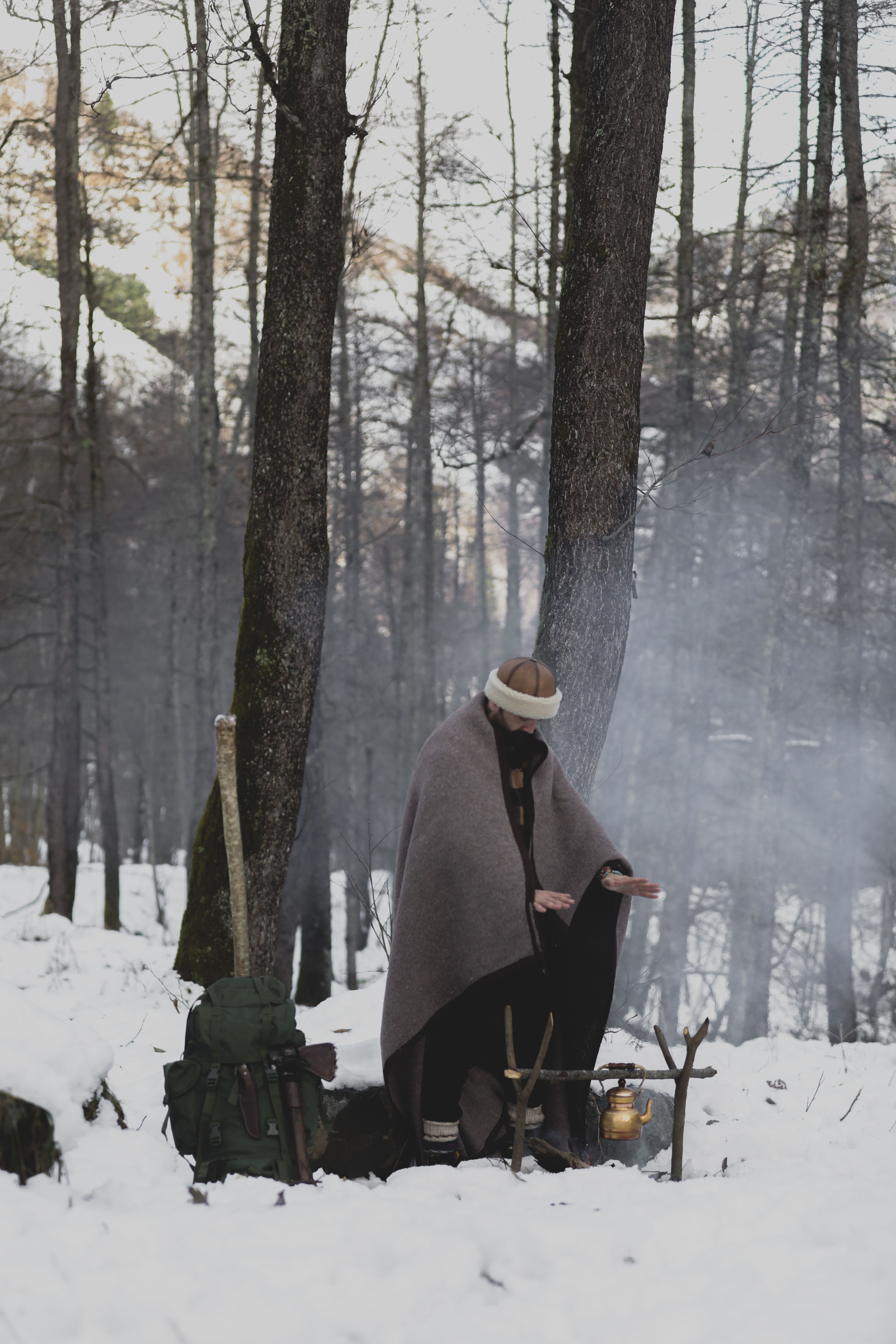 A person wrapped in a blanket for warmth in a snowy forest
