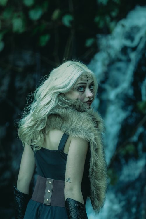 Free A woman dressed in fur and leather poses in a mysterious forest, evoking a fantasy theme. Stock Photo