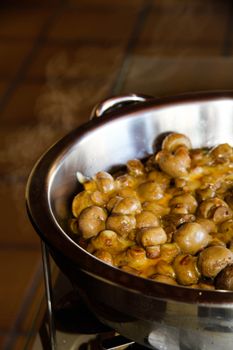 Close-up of sautéed brown mushrooms with melted cheese in a stainless steel pan, showcasing a warm and appetizing meal.
