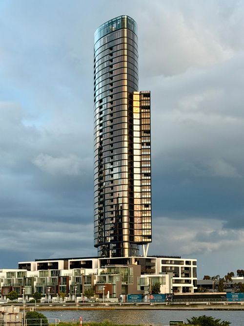 Free A sleek skyscraper stands tall against a clouded sky in Docklands, Victoria. Stock Photo