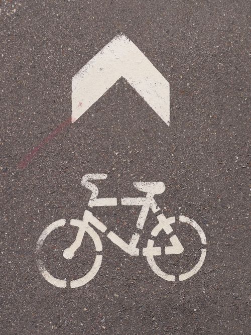 Free White bicycle and arrow markings on an asphalt road surface indicating cycling path. Stock Photo