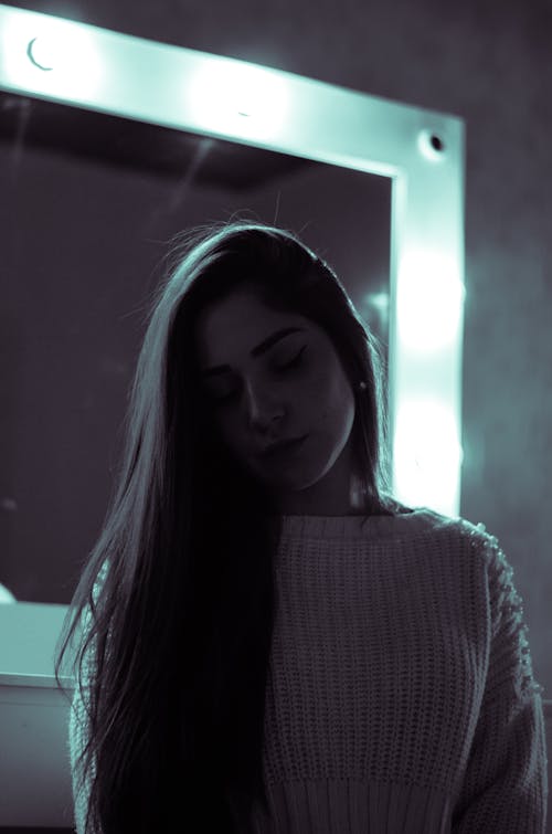 Pensive young woman resting in dark studio against makeup mirror