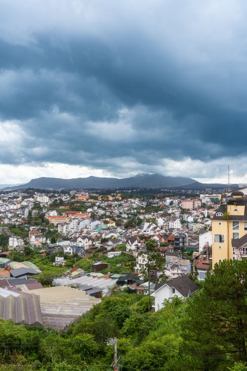 Free Scenic panoramic view of Da Lat city with lush greenery and looming clouds. Stock Photo