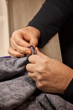 Detailed shot of hands repairing a zipper on patterned fabric indoors.