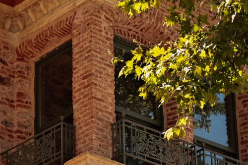 Free A sunlit brick building corner with intricate railing and vibrant green leaves. Stock Photo