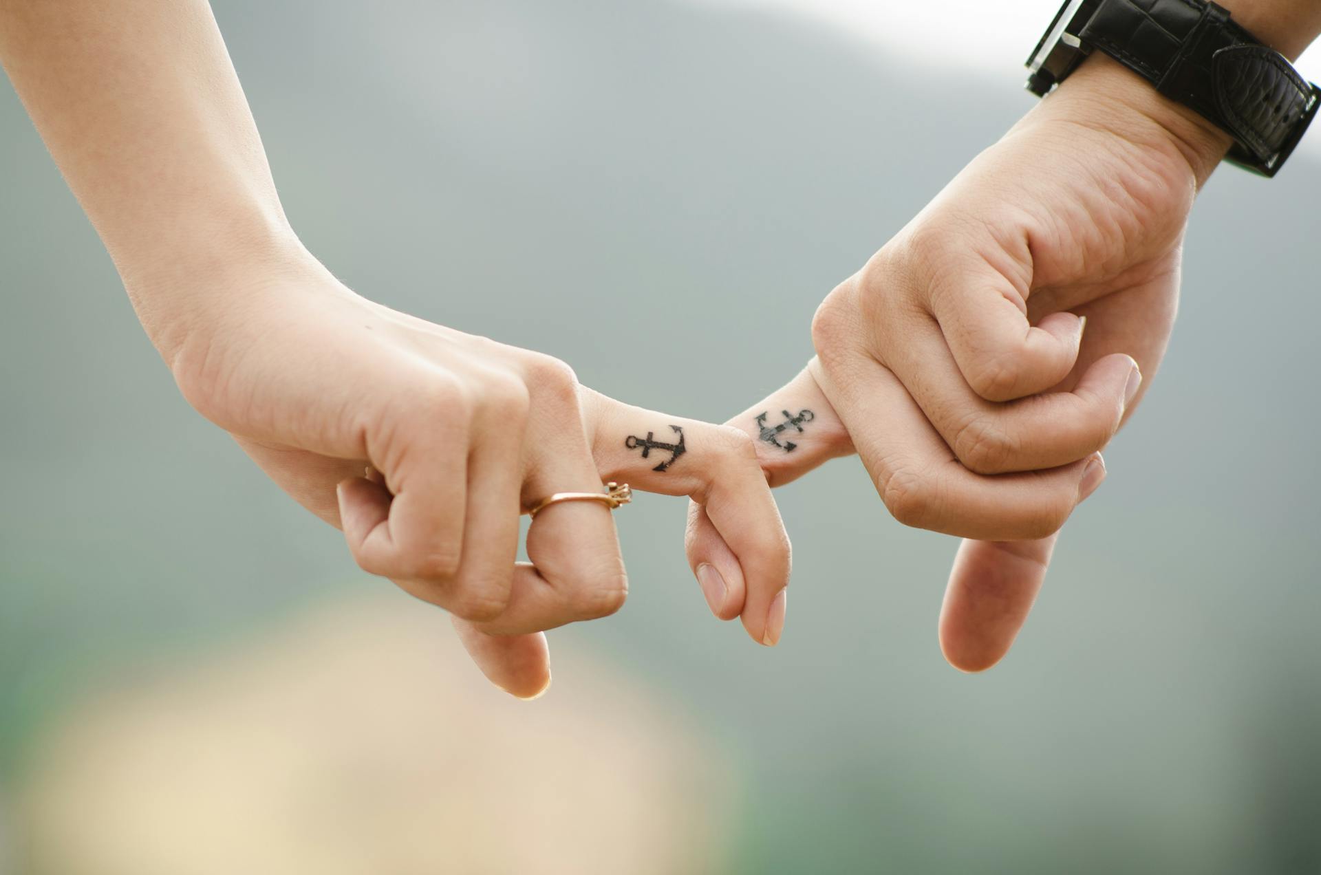 Close-up of a couple holding hands, featuring anchor tattoos symbolizing love and connection.