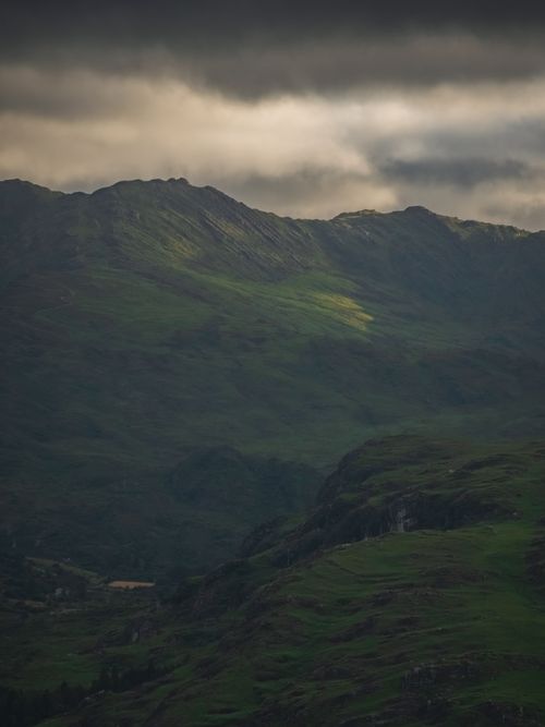 Free Cloudy skies cast shadows over a lush, green mountain range in Ireland, creating a dramatic and moody scene. Stock Photo