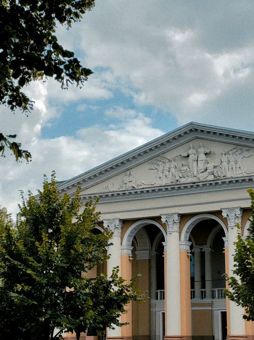 Free A neoclassical building with detailed sculptures and grand columns under a cloudy blue sky. Stock Photo