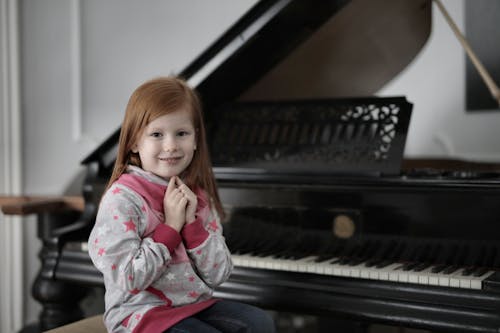 Free Girl in Gray and Pink Jacket Playing Piano Stock Photo