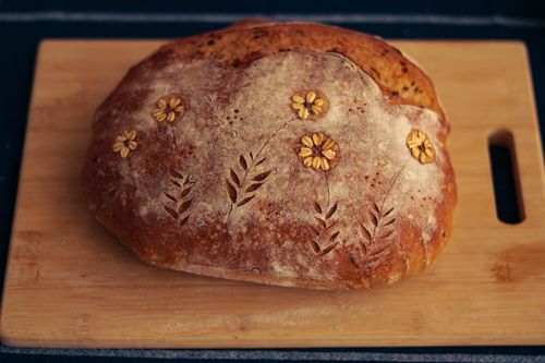 Free Close-up of artisan bread with intricate floral design on wooden board, ideal for bakery promotions. Stock Photo