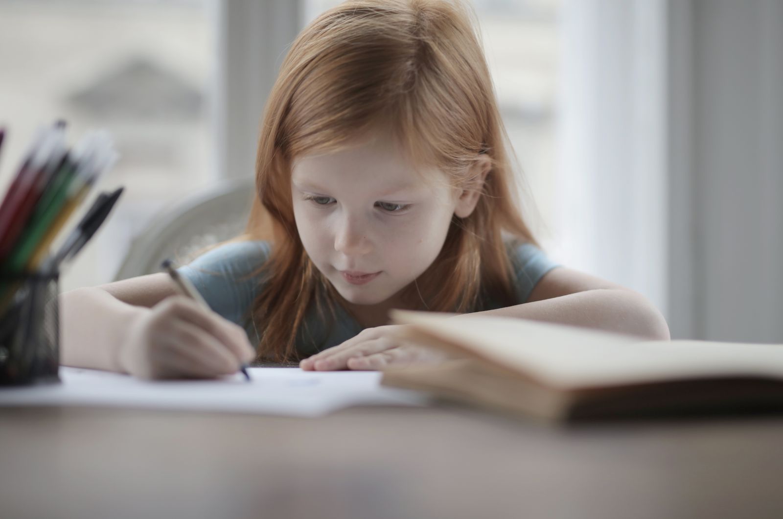 A child writing calmly at a table by a window.