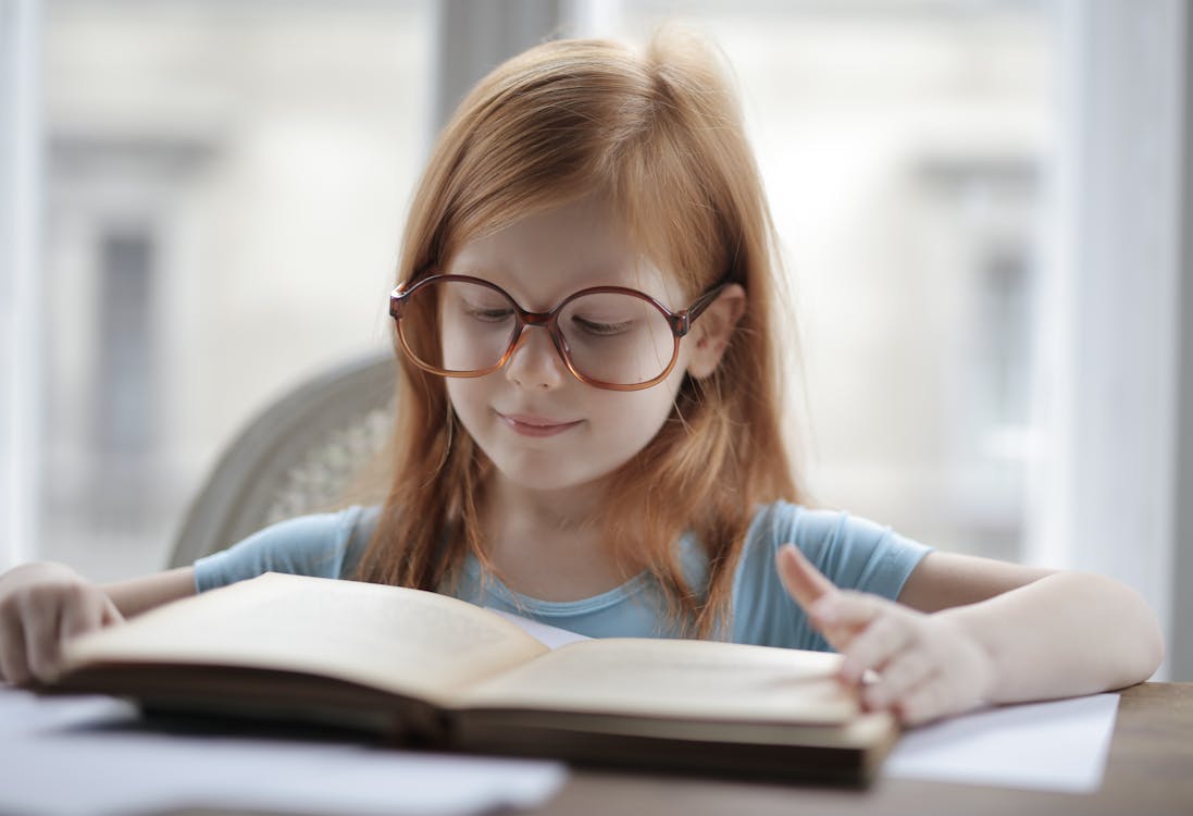 Free Girl In Blue Shirt Wearing Eyeglasses Reading A Book Stock Photo