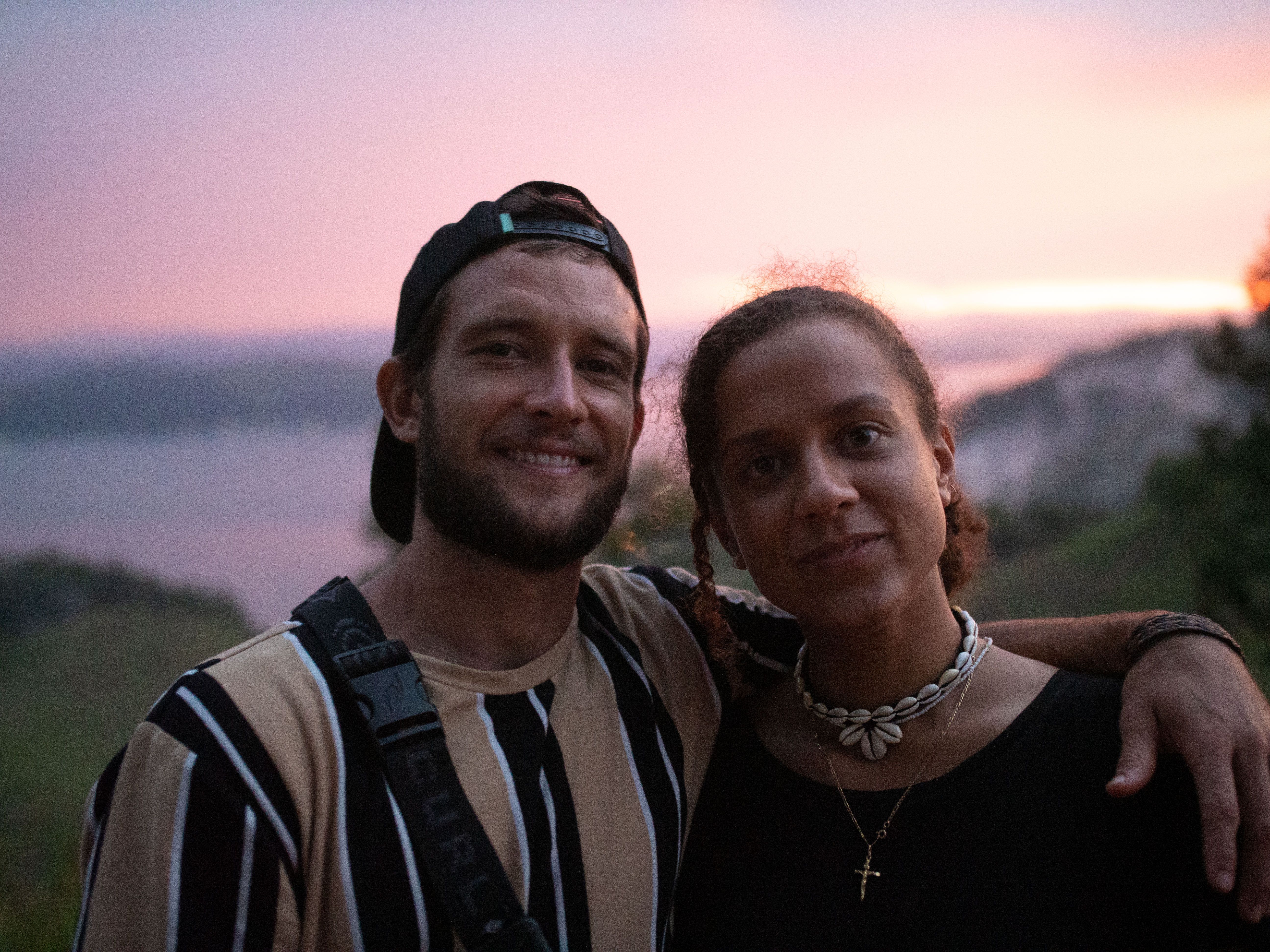 A happy couple poses at sunset with a scenic lake view, capturing a warm moment.