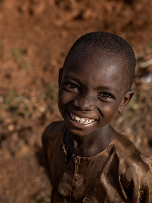 Free A happy child smiles brightly outdoors against a natural earthy backdrop. Stock Photo